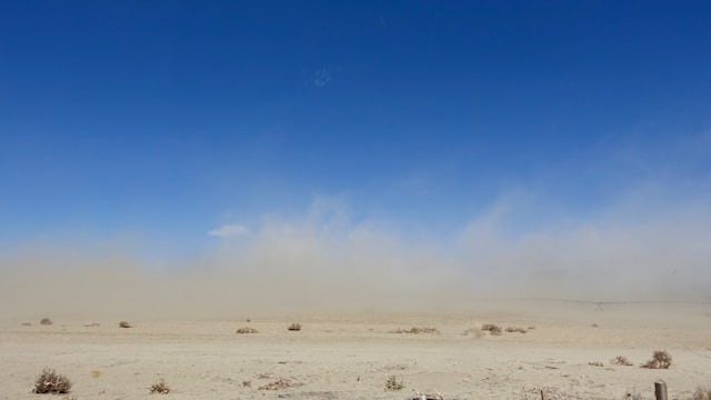 Wide desert scene under a clear blue sky, showing arid terrain and dust-prone conditions.
