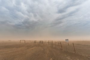 Wire fence cutting across a barren desert landscape with dry soil and sparse vegetation, symbolizing drought and land degradation.