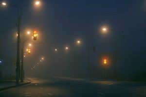 Street at night covered in thick fog with glowing street lights, illustrating low visibility and driving hazards.