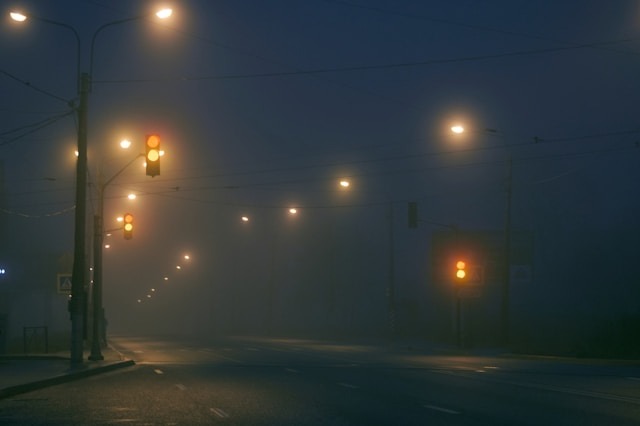 Street at night covered in thick fog with glowing street lights, illustrating low visibility and driving hazards.