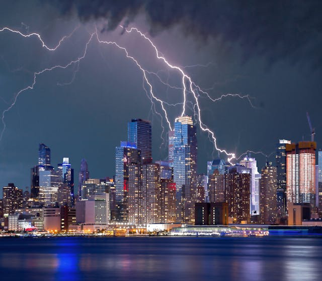 City skyline illuminated at night with lightning flashing above, highlighting urban vulnerability during thunderstorms.